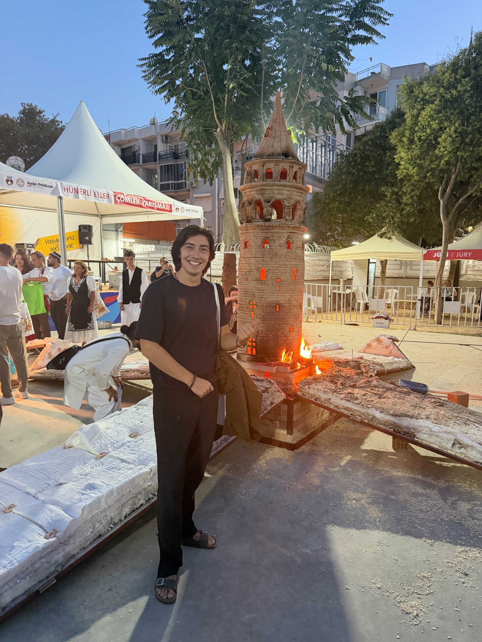 Daniel smiling beside a monumental ceramic tower as flames rise from its base