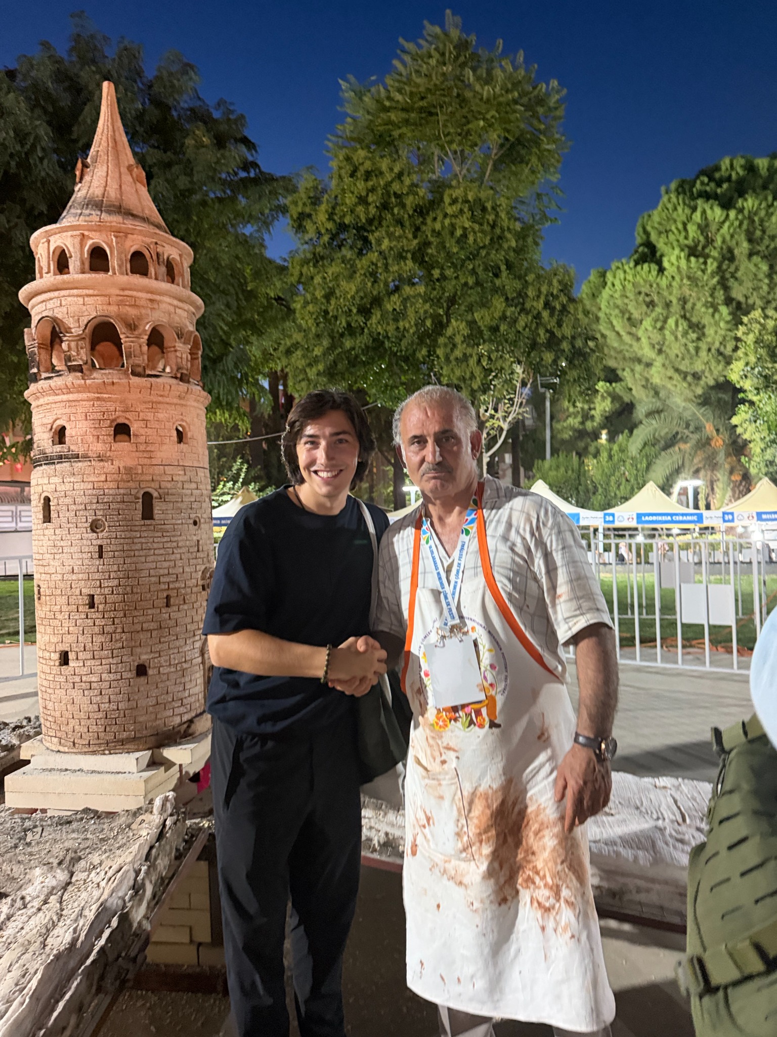 Daniel shaking hands with a ceramic artist beside the fired tower